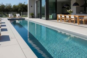 A sleek inground lap pool beside a modern Sydney home, featuring poolside lounge chairs and an outdoor dining area with glass fencing.