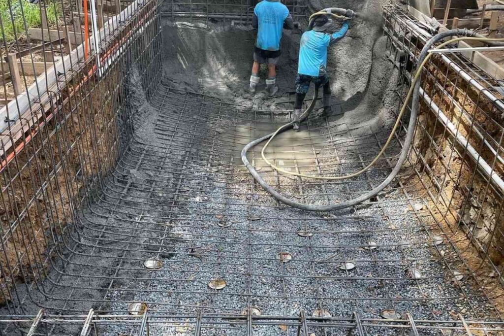 Two workers applying shotcrete on the pool