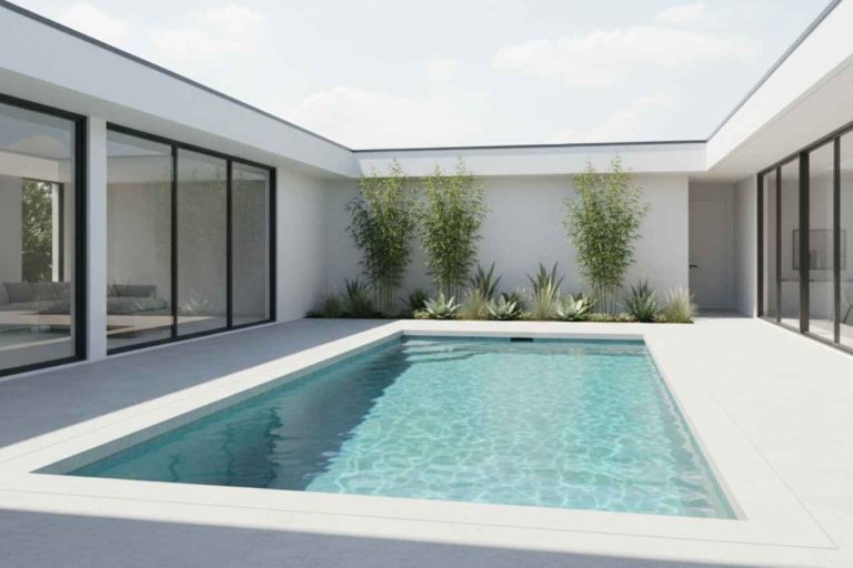 Minimalist courtyard with a rectangular concrete plunge pool surrounded by smooth grey concrete decking, modern white house walls, glass sliding doors, and bamboo plants along the garden bed.
