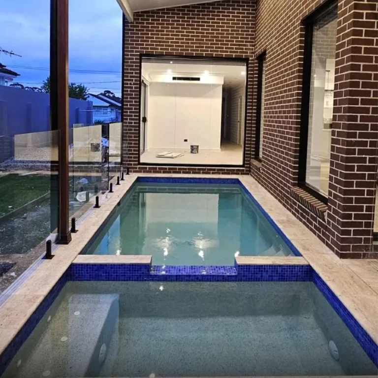 Narrow custom plunge pool beside modern brick home with glass fencing and tiled finish