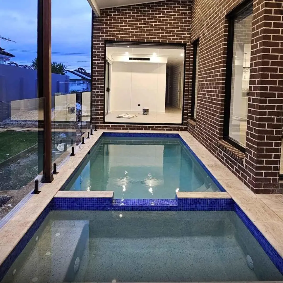 Narrow custom plunge pool beside modern brick home with glass fencing and tiled finish