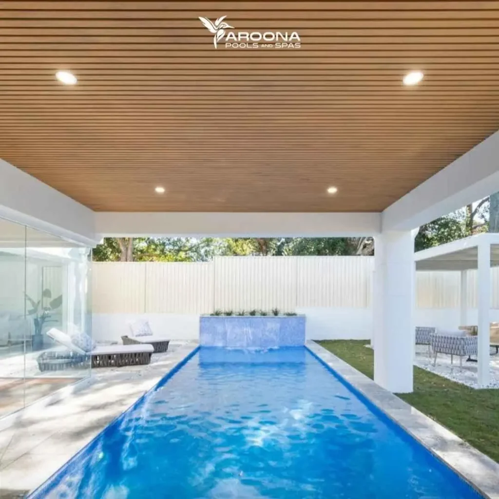 Custom lap pool under modern covered patio with timber ceiling and water feature wall