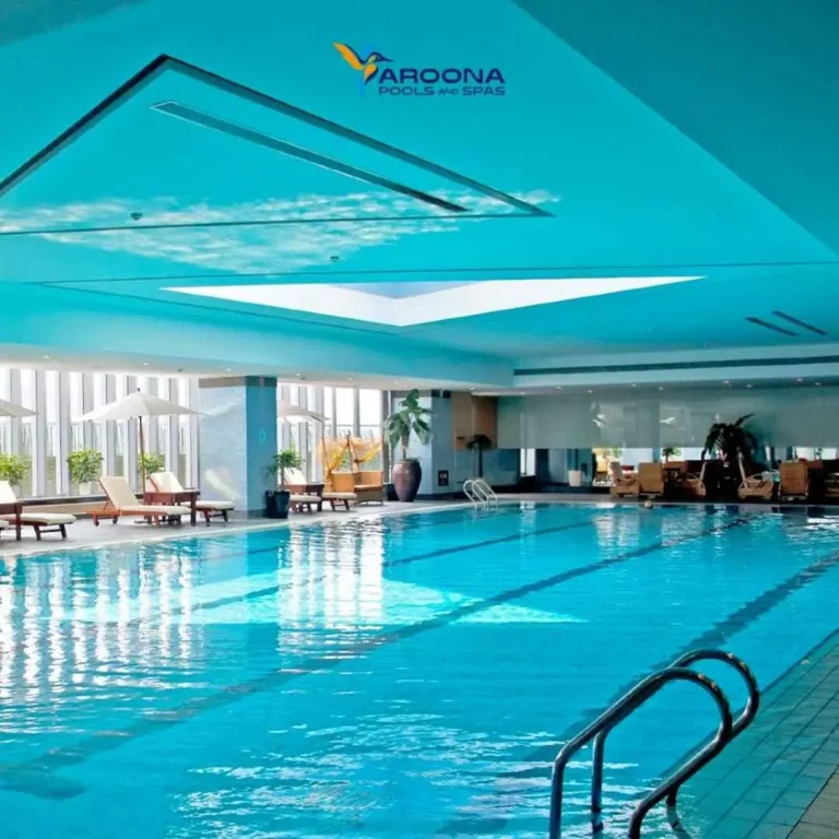 Indoor lap swimming pool with lounge chairs and large windows in a modern facility