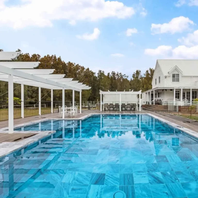 Large rectangular lap pool with white pergola and outdoor seating area in spacious backyard