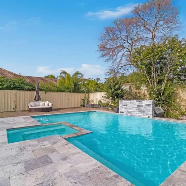 Large backyard swimming pool with spa section, stone water feature, and landscaped garden