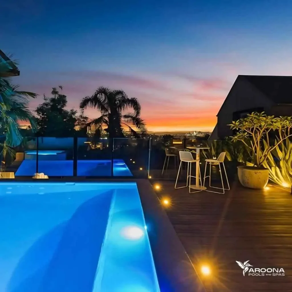 Luxury swimming pool at sunset with LED lighting, timber deck, and outdoor seating area