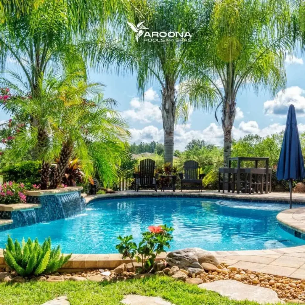 Tropical-style freeform swimming pool with palm trees, waterfall feature, and landscaped garden