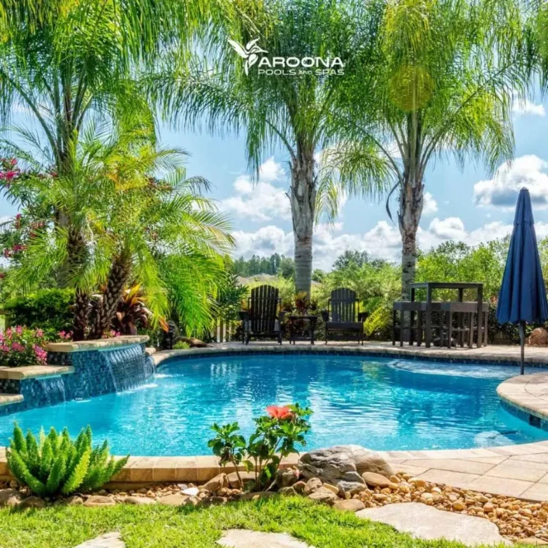 Tropical-style freeform swimming pool with palm trees, waterfall feature, and landscaped garden