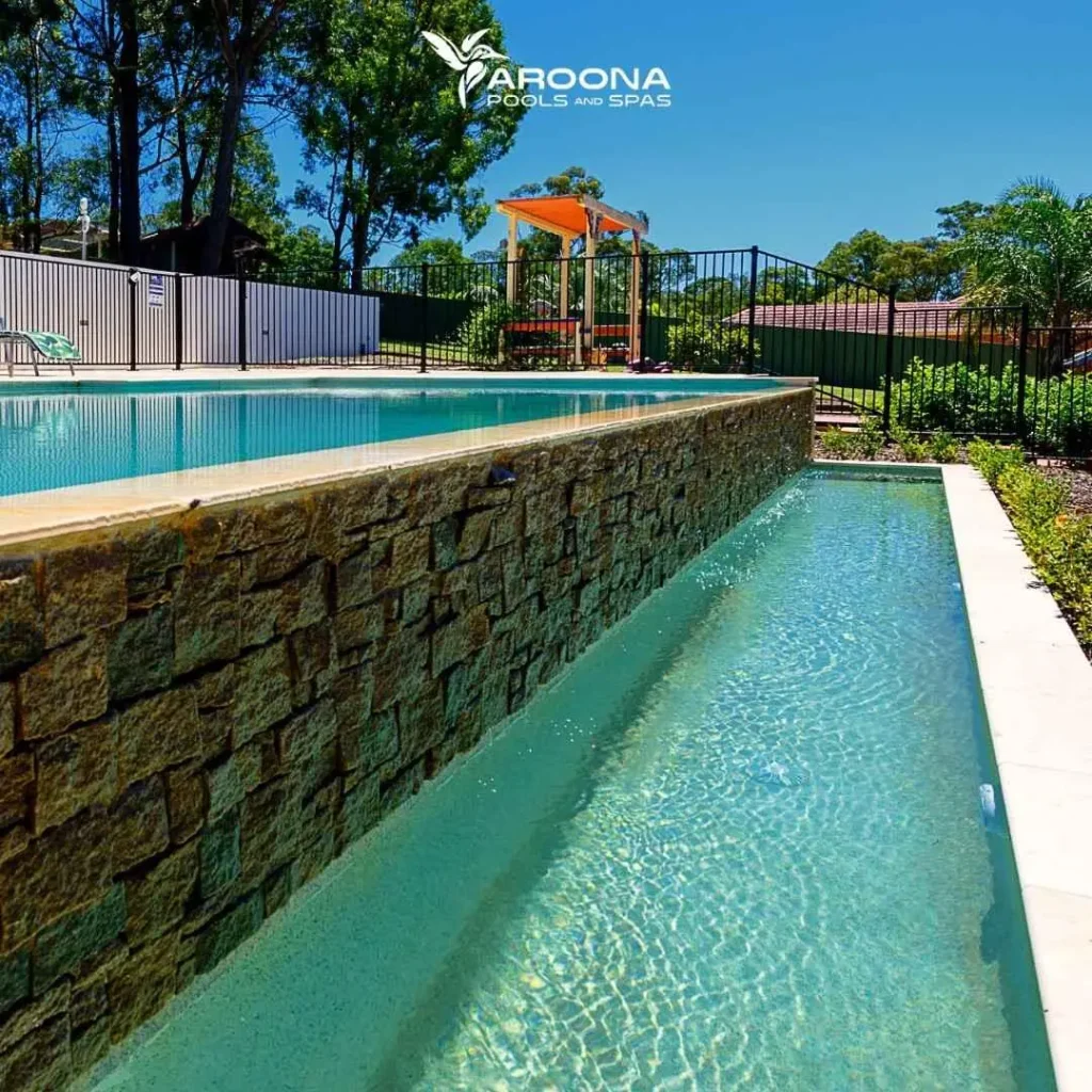 Infinity-edge swimming pool with raised stone wall and lower water channel feature
