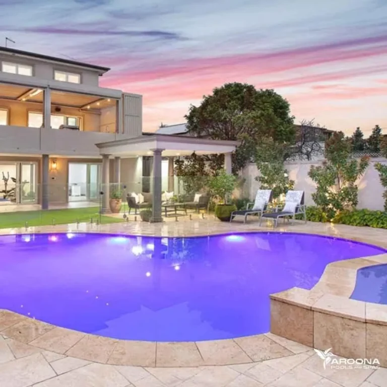 Luxury curved concrete swimming pool with ambient lighting in a modern backyard at sunset